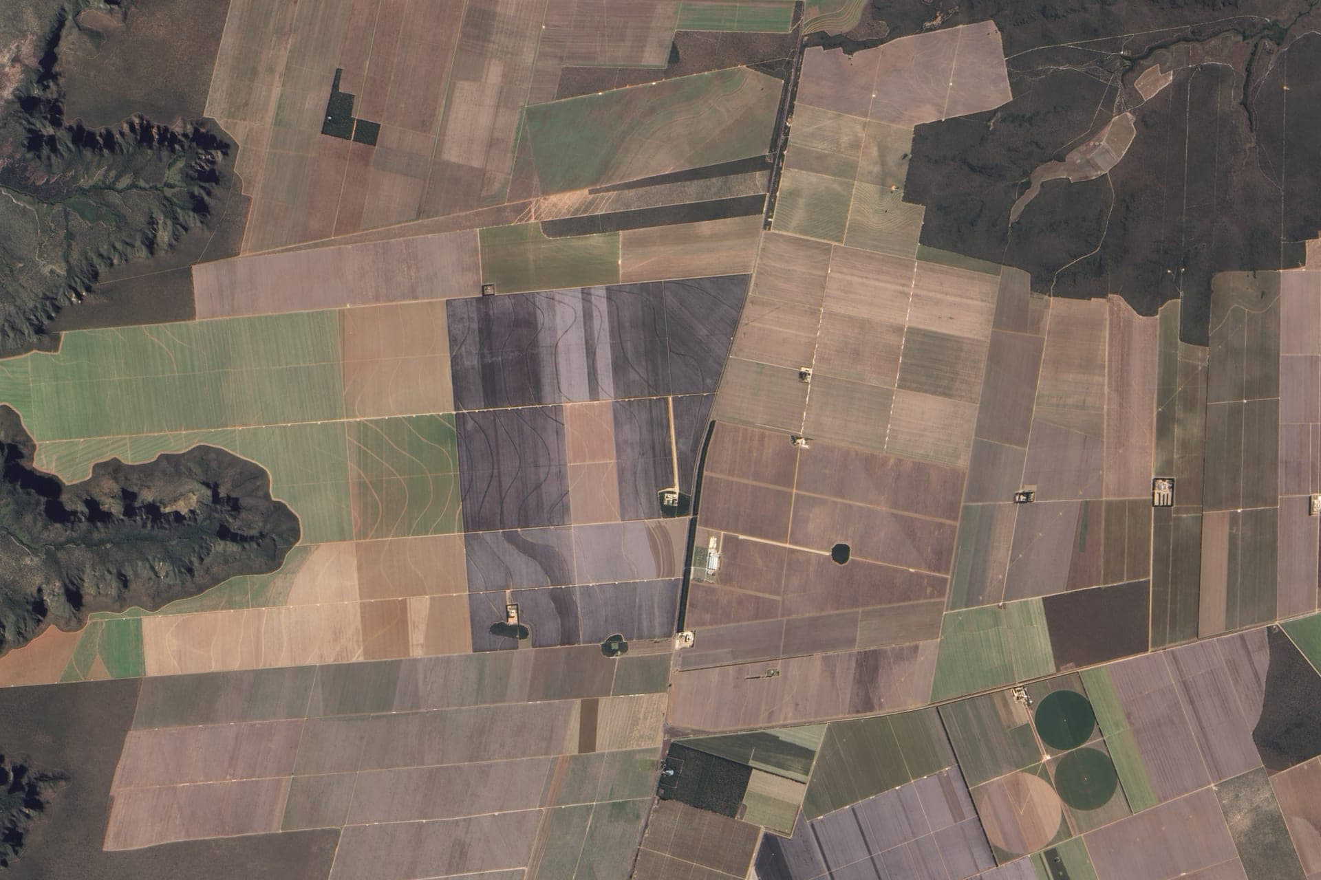 Satellite view of farmland near Luís Eduardo Magalhães in western Bahia, Brazil: earth-toned fields, contour banks that hold the soil, and the plateau's escarpment on the left.